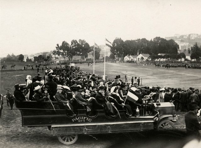 A parade field and grandstands, with an open bus carrying members of San Francisco's Dutch colony