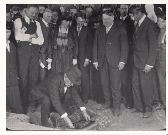 Thomas Edison placing a plaque in the ground, watched by Mina Edison and Harvey Firestone