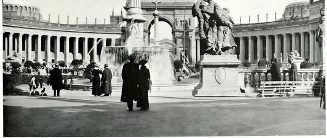Visitors by a fountain in the Court of the Universe, the Arch of the Rising Sun behind