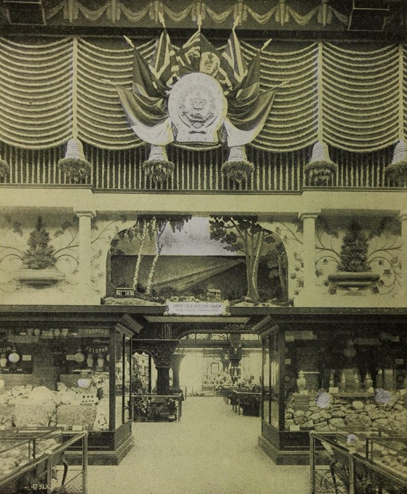 Inside the Canadian Pavilion: a crest and Union Jacks over a diorama of a western wheat field, with mineral cases on either side